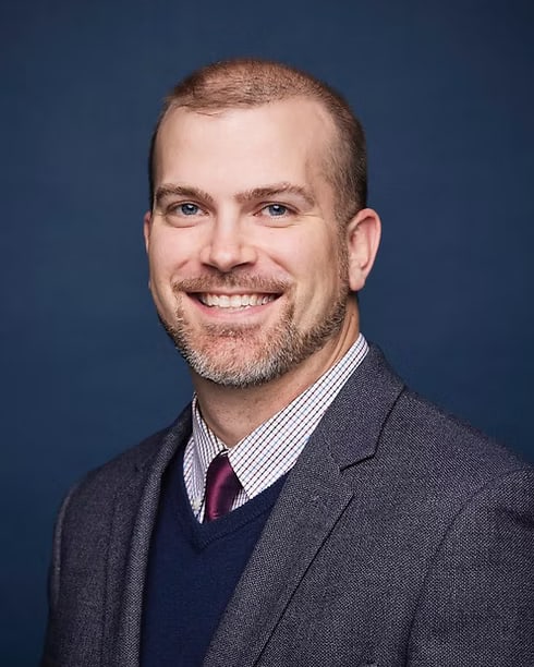 C. Denny King, DNP, APRN, PMHNP-BC, smiling, in a grey jacket and navy sweater